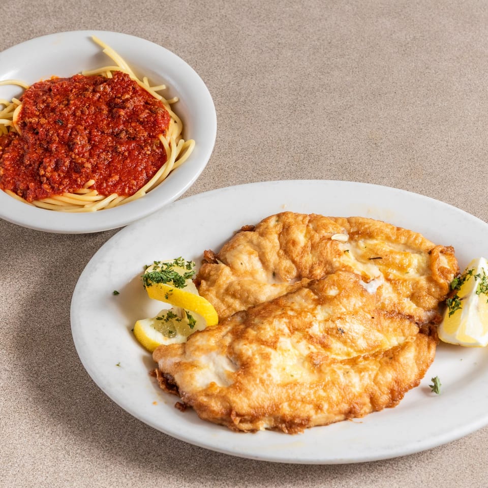 Two golden-brown fried cutlets with lemon wedges and parsley, next to a bowl of spaghetti with red sauce.